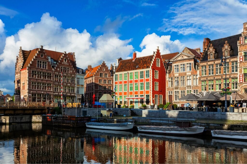 Kleurrijke historische gebouwen langs de Leie in Gent, België, weerspiegeld in het water onder een heldere blauwe lucht — waar De Schoonmaakberen professionele schoonmaakdiensten aanbiedt.